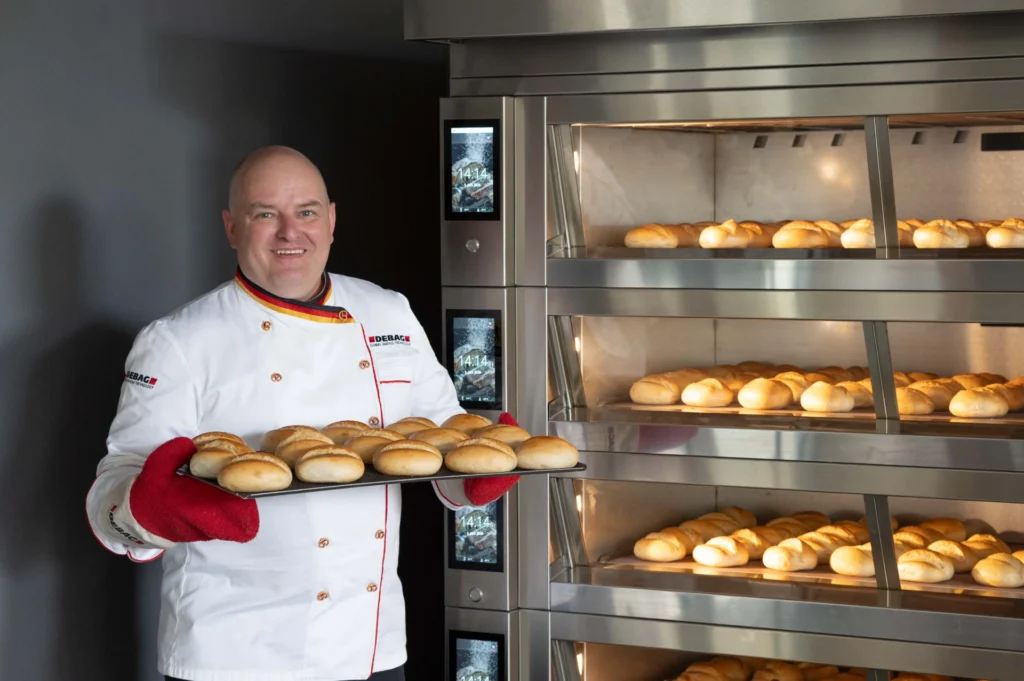 Boulanger présentant un plateau de pains devant un four ventilé DEBAG